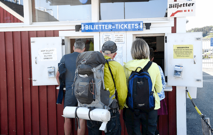 Några personer med ryggsäckar står framför luckan till biljettkontoret i Köpmanholmen. 